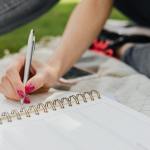 crop female noting down daily plans in notebook in park
